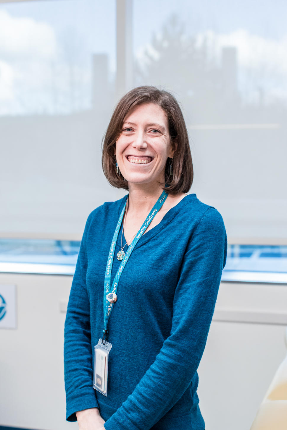Woman with shoulder length brown hair wearing a blue blouse, necklace, and Seattle Children’s lanyard.