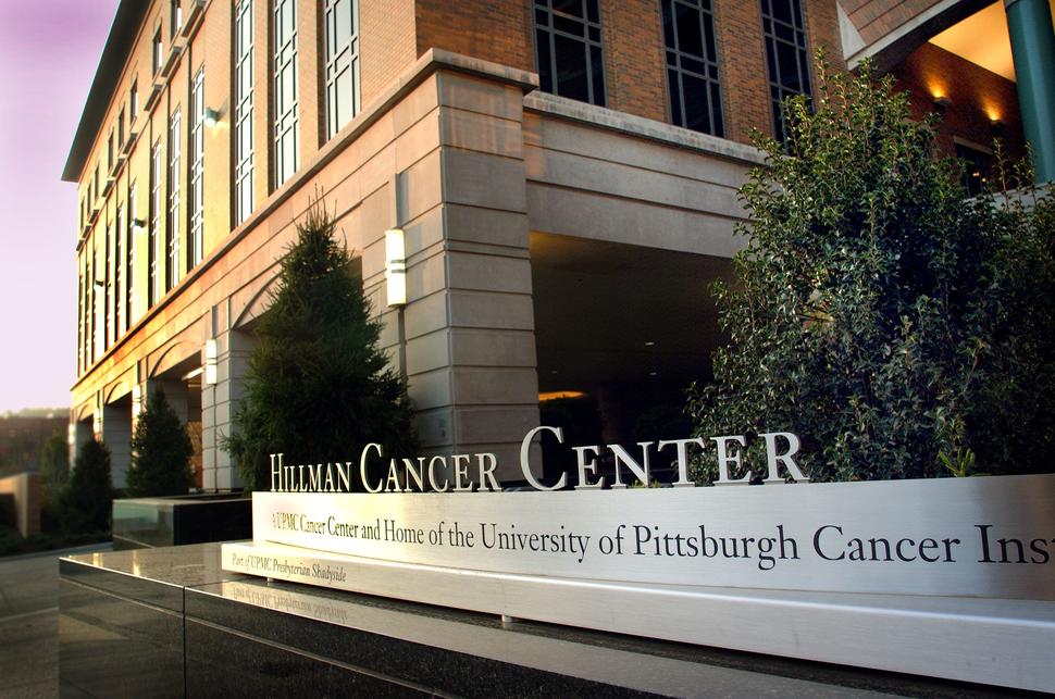 Exterior photo of the University of Pittsburgh Cancer Institute. The sign of the institute is in the foreground with part of the building in the background. 