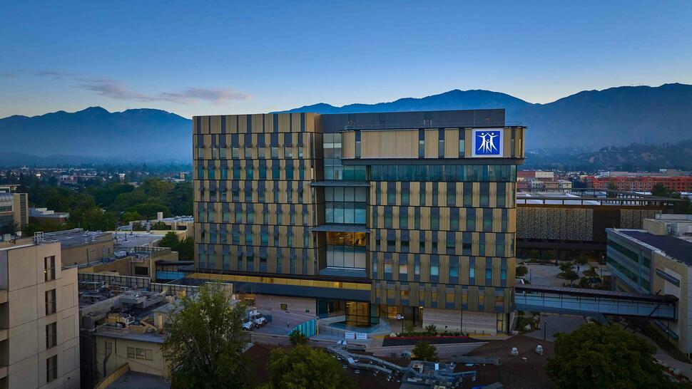 City of Hope Comprehensive Cancer Center building with patterned facade, set against mountains at dusk.