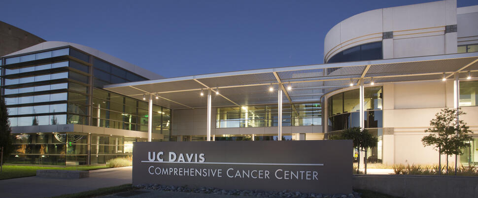 UC Davis Comprehensive Cancer Center entrance with illuminated sign and modern glass buildings at dusk.