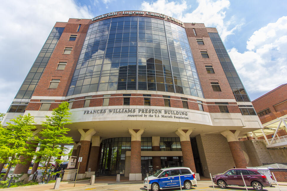 Vanderbilt-Ingram Cancer Center building with a curved glass facade and brick exterior, viewed from street level under a partly cloudy sky.