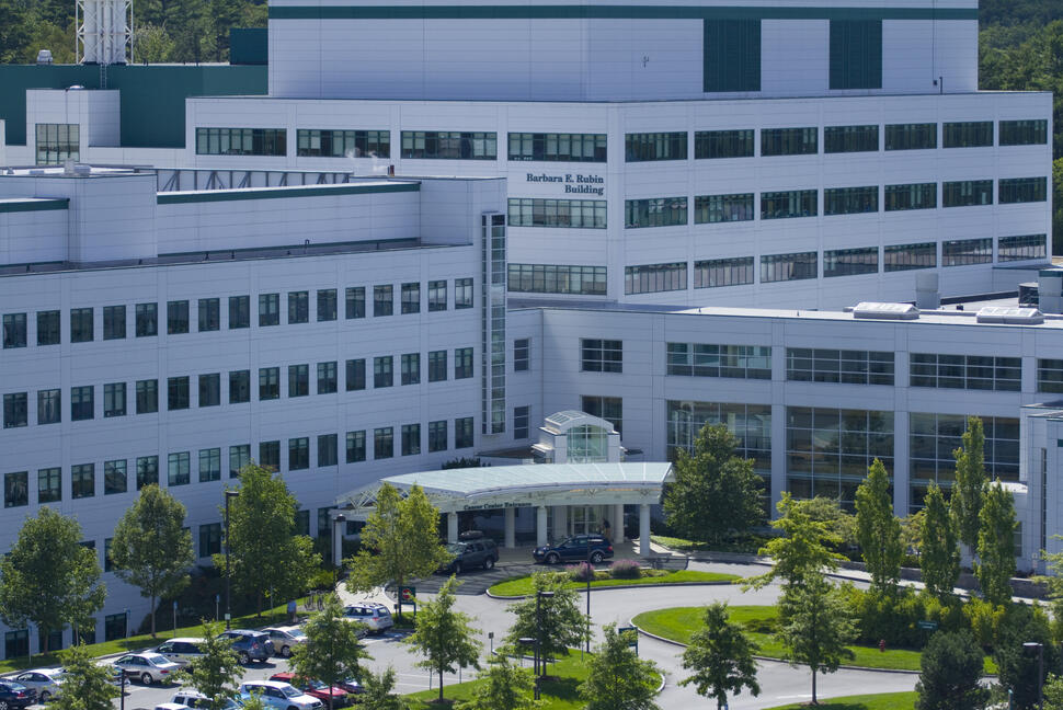 Norris Cotton Cancer Center at Dartmouth-Hitchcock Medical Center, a large white building with rows of windows, a covered entrance, and surrounding trees.