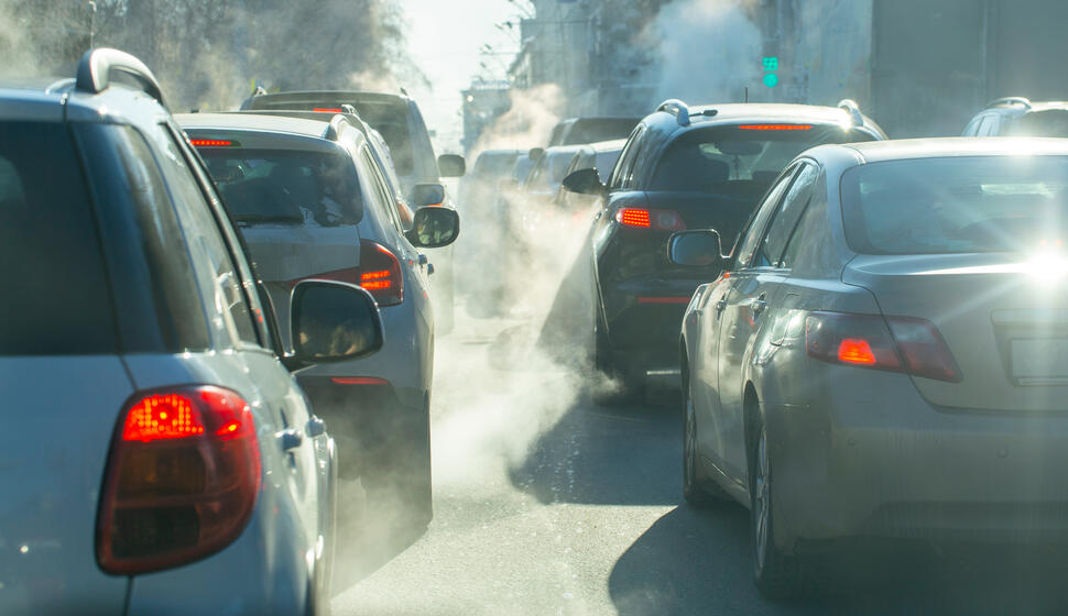 Traffic congestion with multiple cars idling on a city street, visible exhaust drifting between vehicles.