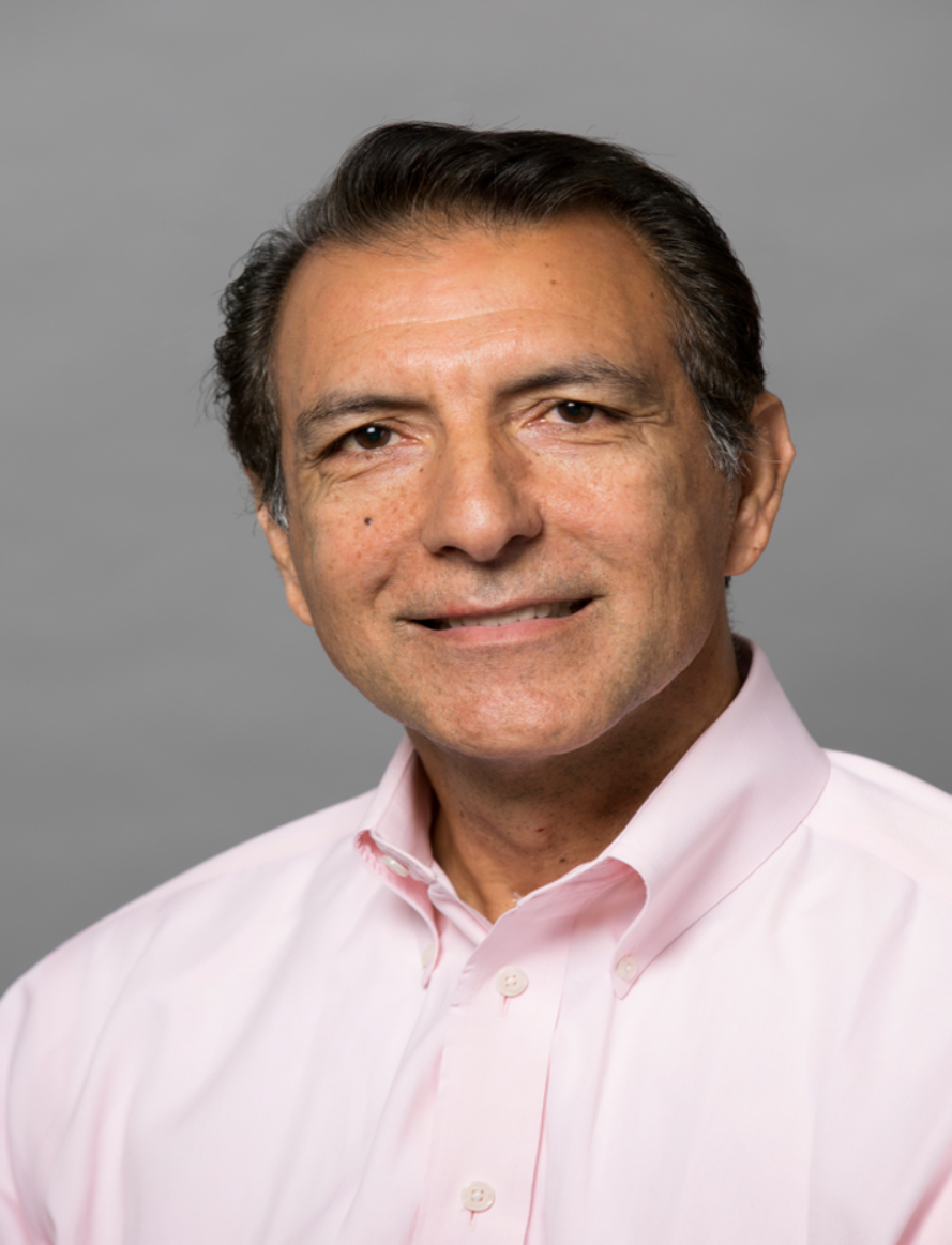 Professional headshot of Dr. Daoud Meerzaman. He's smiling at the camera dress in a pink button-down shirt against a gray backdrop.