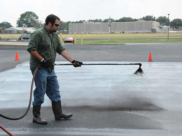 Man spraying coal-tar pitch onto asphalt