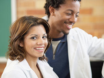 A smiling man and woman wearing white lab coats.