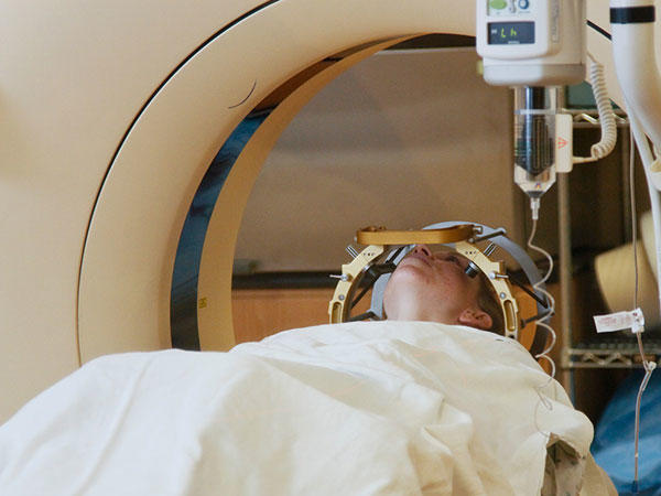A patient covered with a white blanket goes into a CT machine.