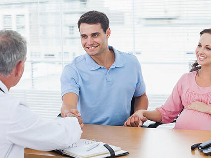 A pregnant person and their partner talking with a doctor at a desk.