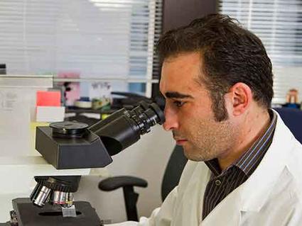 Scientist in white lab coat examining samples through a microscope in a laboratory setting.