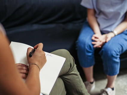 Therapist taking notes during a session with a cancer patient, shown seated with hands clasped