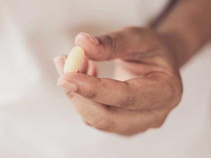 Close-up of hands holding a yellow pill against a white background.