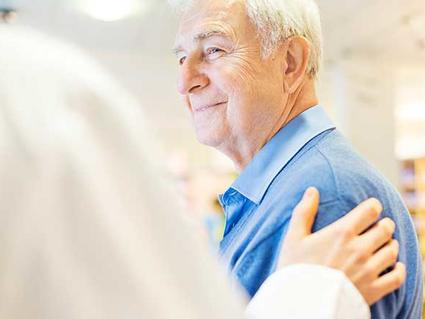 A doctor puts his hand on an older man's shoulder.