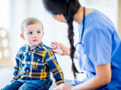Female health care provider talks to young boy seated next to her.