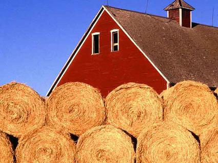Roof of a red farmhouse with hay bales in the foreground.