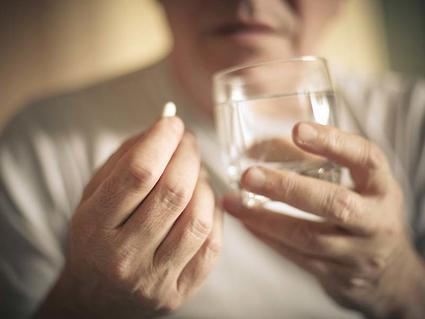 A person with oral medication in one hand and a glass of water in the other hand.