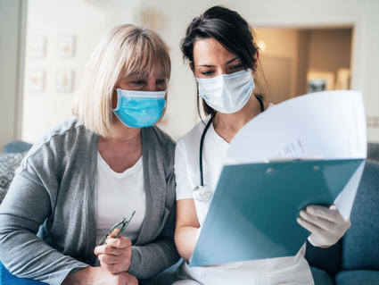 A nurse wearing a face mask talking with an older female patient wearing a face mask.