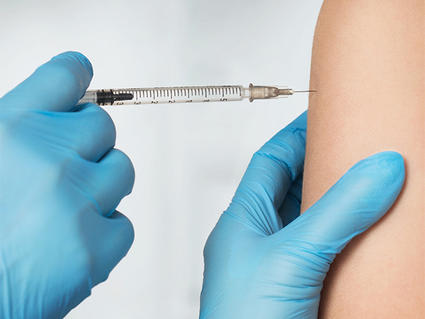 Photo of gloved hands administering an injection into a patient's upper arm.