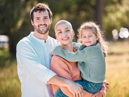 Cancer survivor holding young daughter in arms with husband hugging them both