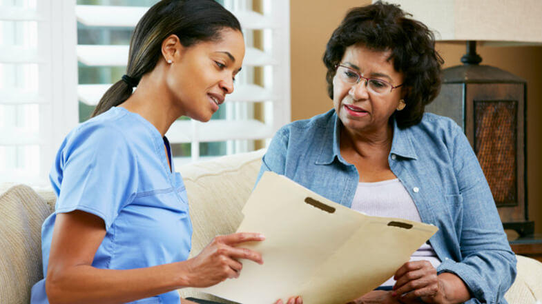 Female nurse and female patient review medical papers together.