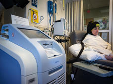 Patient seated in a hospital chair wearing a DigniCap scalp cooling system.
