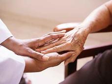 Healthcare provider in white uniform holding an elderly patient's hands in a gesture of comfort and support.