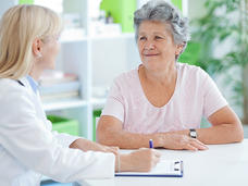 Medical professional writing notes and talking to a patient.