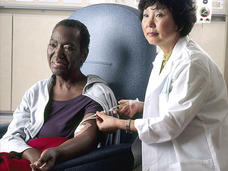 Seated female patient receives chemotherapy infusion from female nurse.