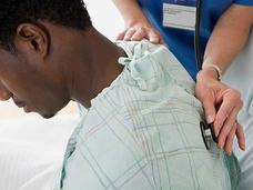 Healthcare provider's hands placing a medical device on a patient's back over their clothing as part of a medical examination or treatment.