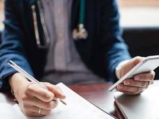 A medical professional writing and using a mobile phone.