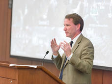 Dr. Norman E. Sharpless speaking at a podium.
