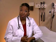 A Black female adult doctor, wearing a white lab coat, red shirt, and stethoscope around her neck, looks at the camera with a serious expression. She is seated next to an examination table. In the background, medical tools hang on the wall.