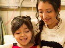 Two sisters sitting side by side reading in a hospital bed