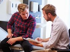 Male doctor talking with male patient in an exam room