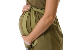 A close-up of a woman’s arms holding her pregnant stomach. She is wearing a dark olive-colored dress.