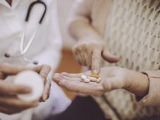 Una mujer mayor con varias pastillas en la mano.