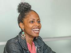 Dr. Lauren E. McCullough, shown sitting, rests her arms on a small stack of books and papers while speaking happily.