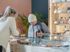 An older woman at a cannabis dispensary looking at products under a glass countertop.