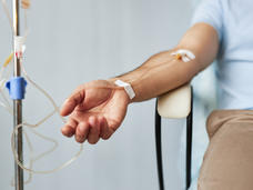 Brazo de un hombre sentado en una silla con una vía intravenosa.