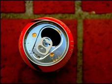 A photo of a red soda can, taken from directly above, sitting on a dark red tiled floor.