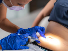 A photograph of a nurse with blue gloves giving a woman an injection of medicine into the lower part of the stomach.