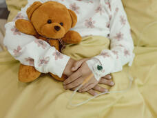 Primer plano de los brazos de una niña que sostiene un oso de peluche mientras recibe una infusión intravenosa