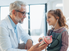 Doctor in white coat with a child patient and stethoscope holding a stuffed animal.