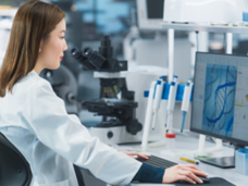 A person in a lab coat, working in a lab on a computer. 