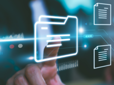 Person sits at a laptop and presses a file. The file opens four documents with a background that shows charts, flow charts, and additional buttons. Signifies the idea of an online resource. 