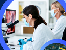 Two women in lab coats and gloves using a microscope.