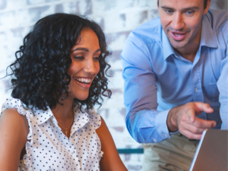 Two people in an office setting looking at an open laptop.