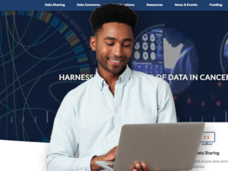 Individual holding a laptop while standing in front of the homepage for datascience.cancer.gov website.