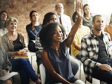 Group of adult students in a classroom studying, with one woman raising her hand.