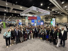 About 70 professionally dressed people smiling at the camera and standing in a semicircle in front of the NCI exhibit booth.