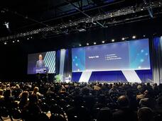 Dr. Anthony Letai stands at a lectern on a stage and addresses attendees filling rows of seats in a large conference hall.